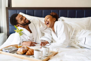 black couple enjoying breakfast in bed in Whitney hotel robe in hotel room photographed by Boston Photographer Nicole Loeb