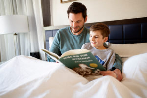 Father and son reading a book in a hotel room photographed by Boston photographer Nicole Loeb
